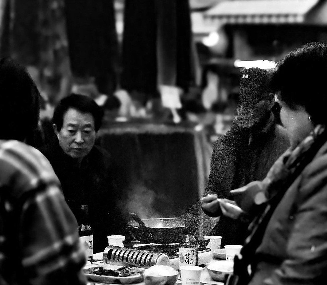 Friends sharing a steaming hot pot at a night market, black and white