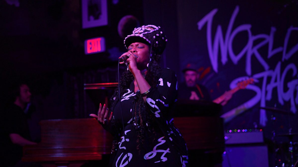 Singer mid-song on the World Stage under purple light, band behind