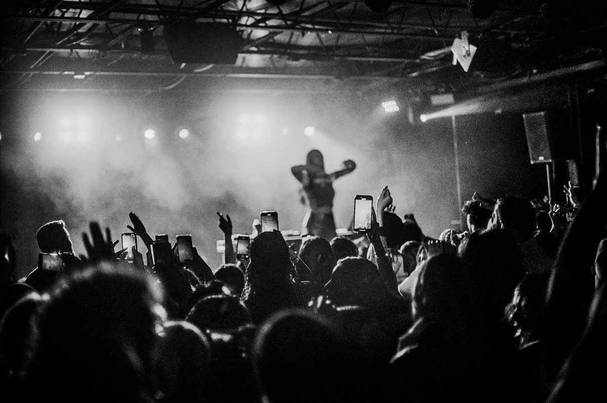 Crowd with phones raised toward a lit stage, black and white