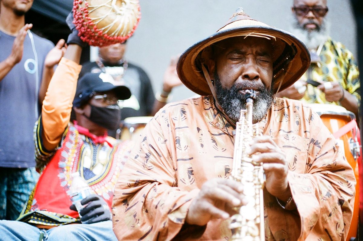 Saxophonist in a woven hat playing in a crowd
