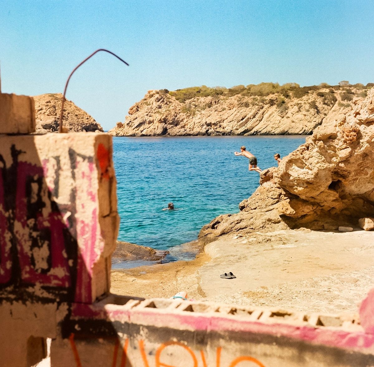 Boy diving off rocks into a turquoise cove, framed by graffiti walls