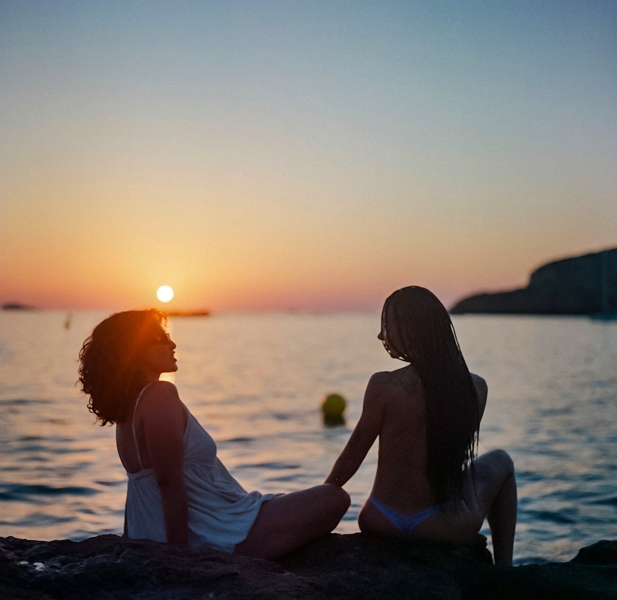 Two women silhouetted on rocks at sunset over the sea