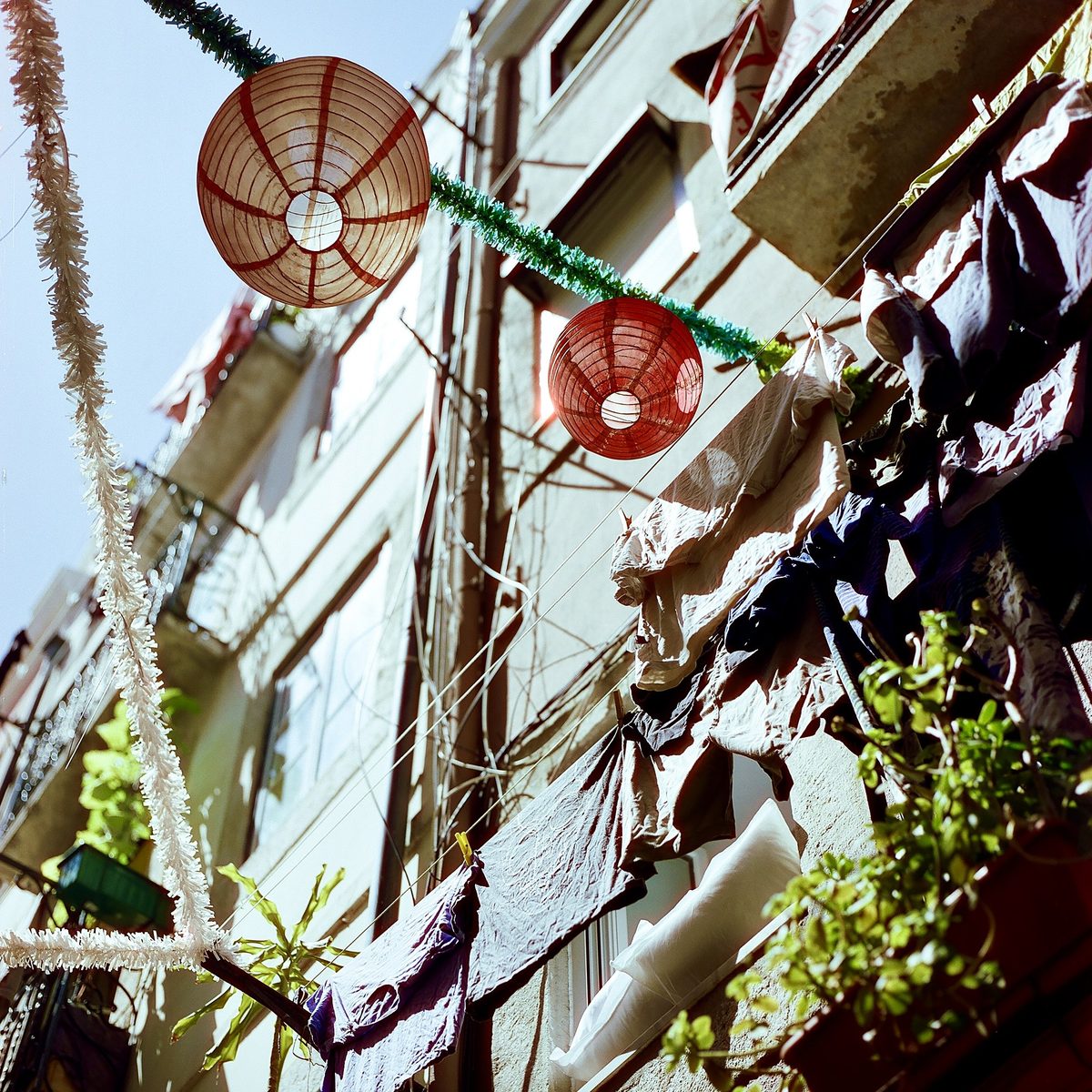 Paper lanterns and laundry strung between balconies, looking up