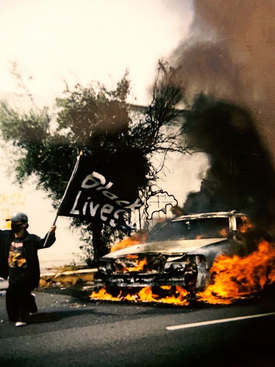 Protester waving a Black Lives Matter flag beside a burning car