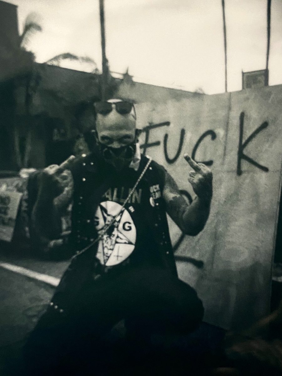 Punk in studs and chains giving the finger before a graffiti wall, sepia